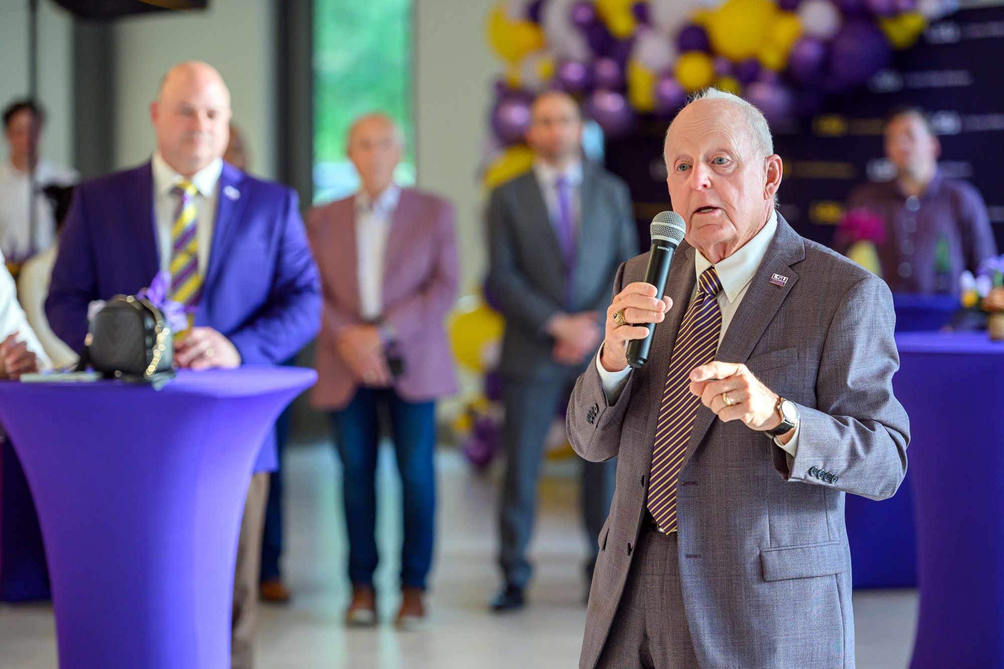 Man speaking into a mic while group of people stand watching